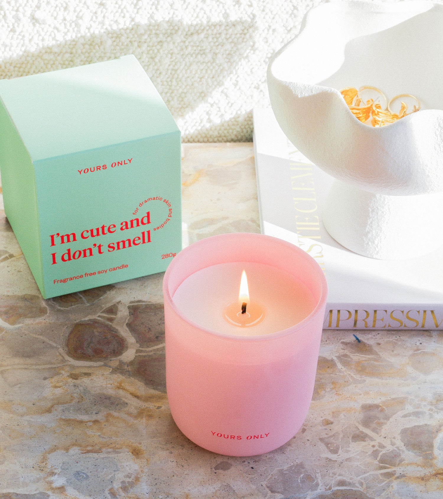Pink candle in a glass jar with a lit wick, next to a mint green box on a marble surface