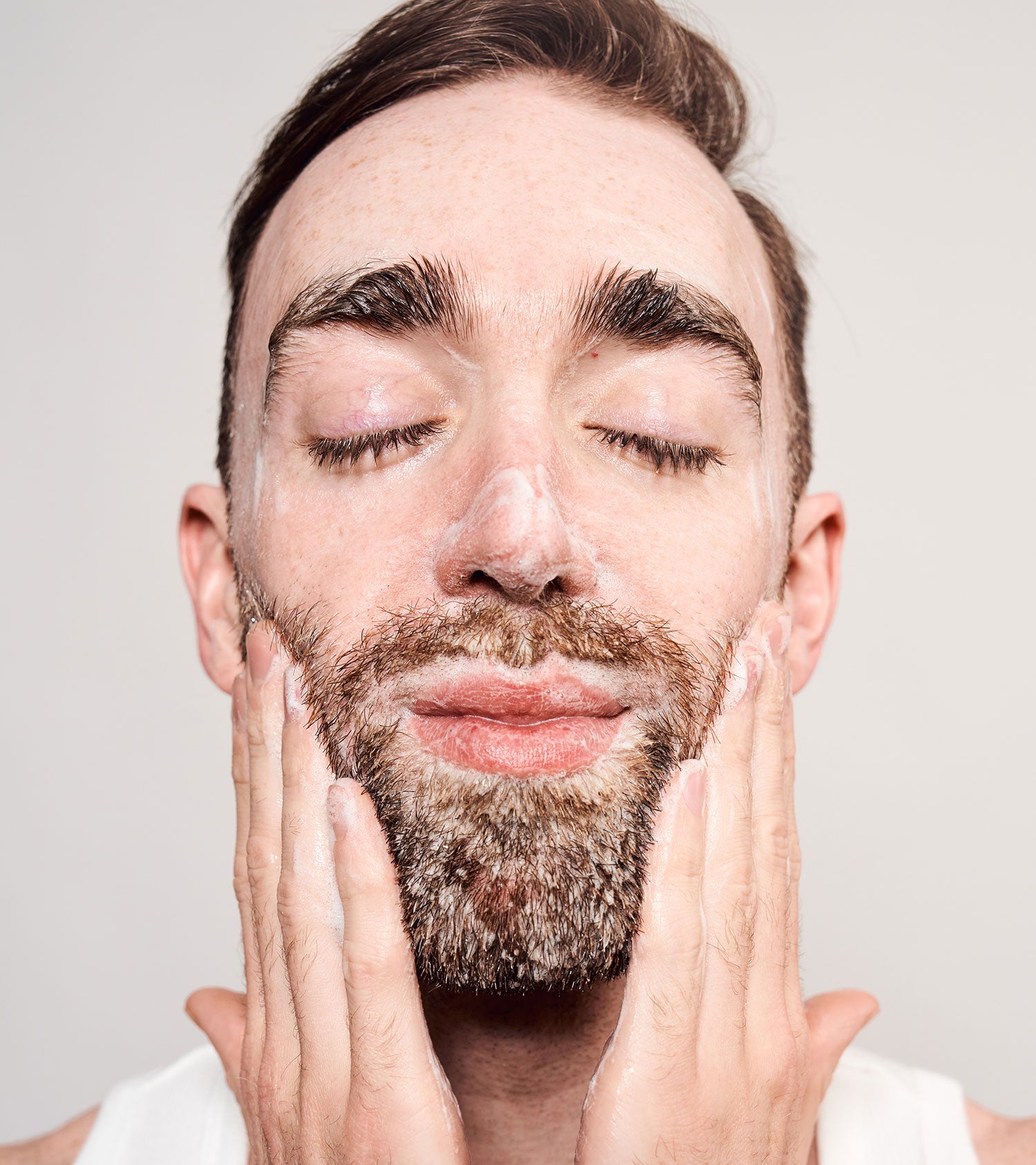 Man with closed eyes washing his face and beard with cleanser from the pre-order starter bundle