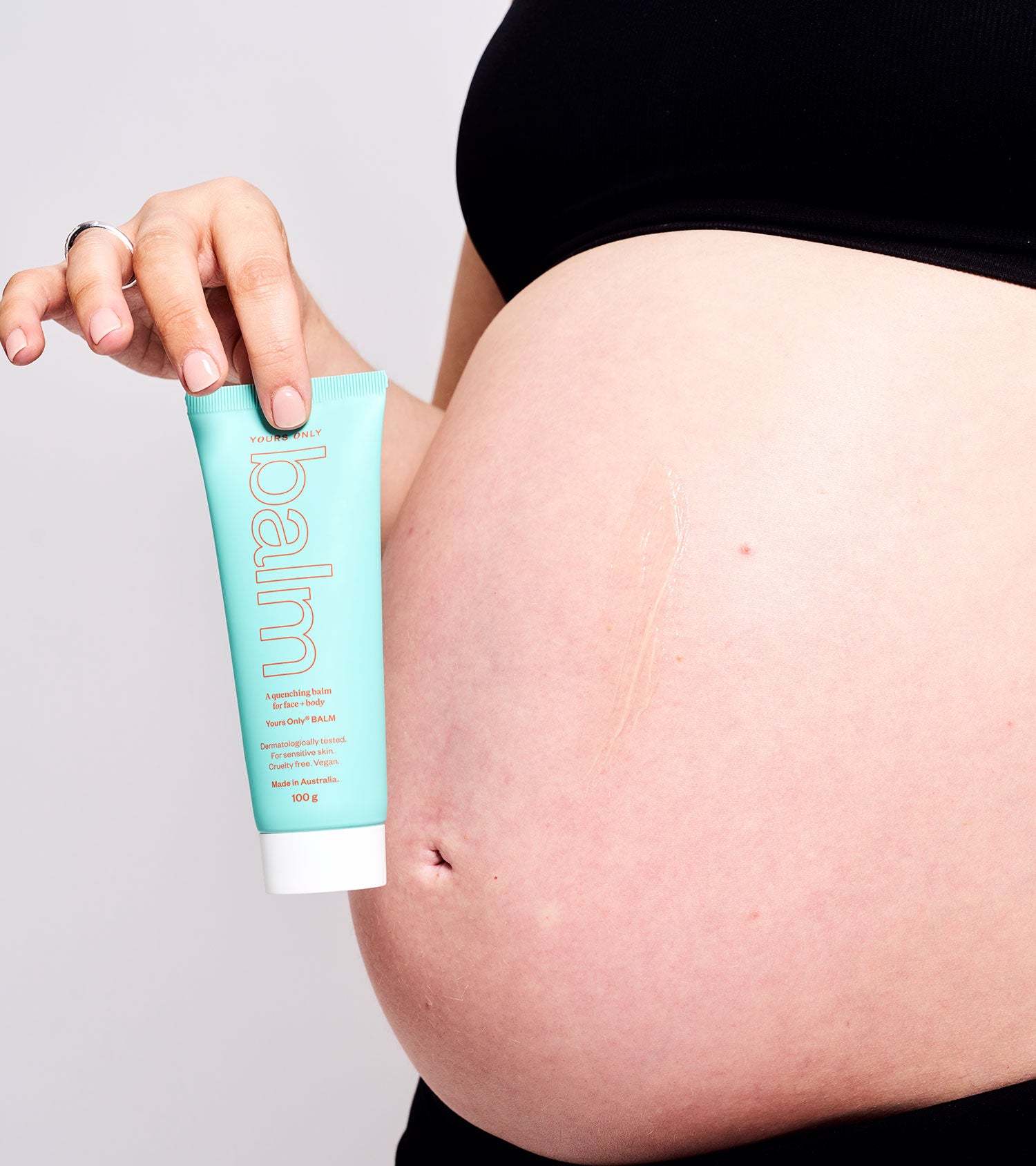 Pregnant person holding lip + body balm 100g GWP, with balm applied to their stomach