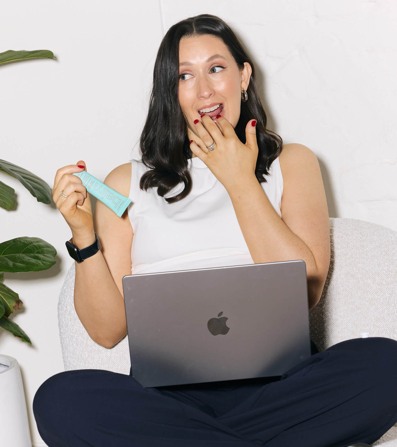 Woman holding lip + body balm 30g, sitting with a laptop