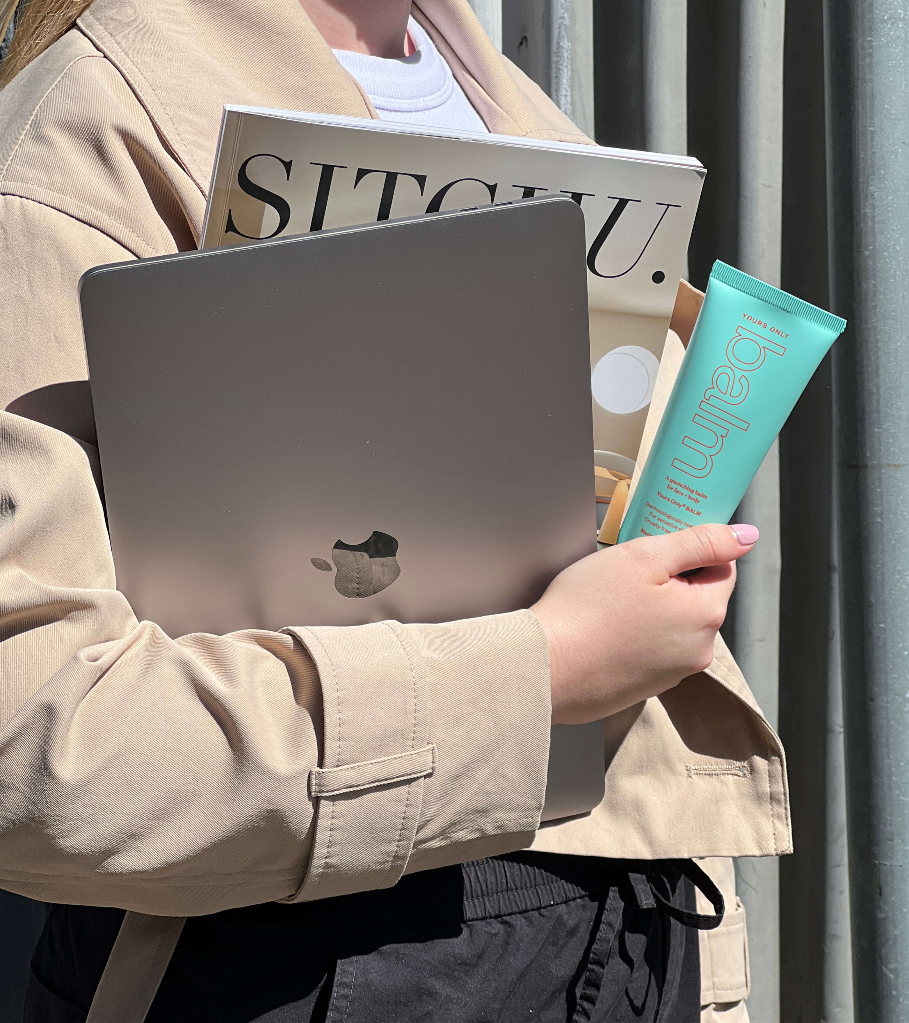 Person holding a laptop, magazine, and a tube of lip + body balm 100g GWP