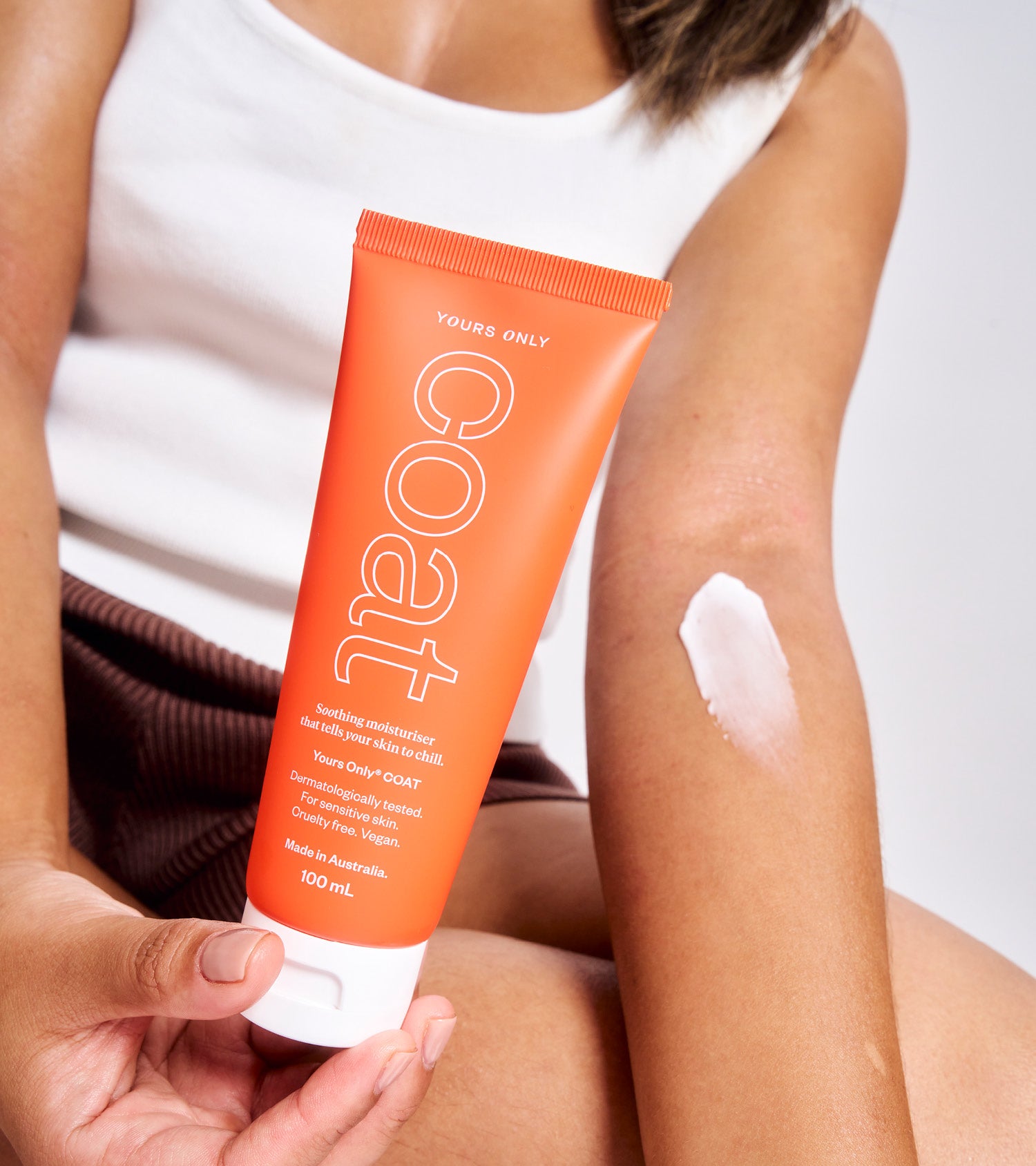 Woman holding a tube of Yours Only COAT 100mL and applying a swatch of cream to her arm