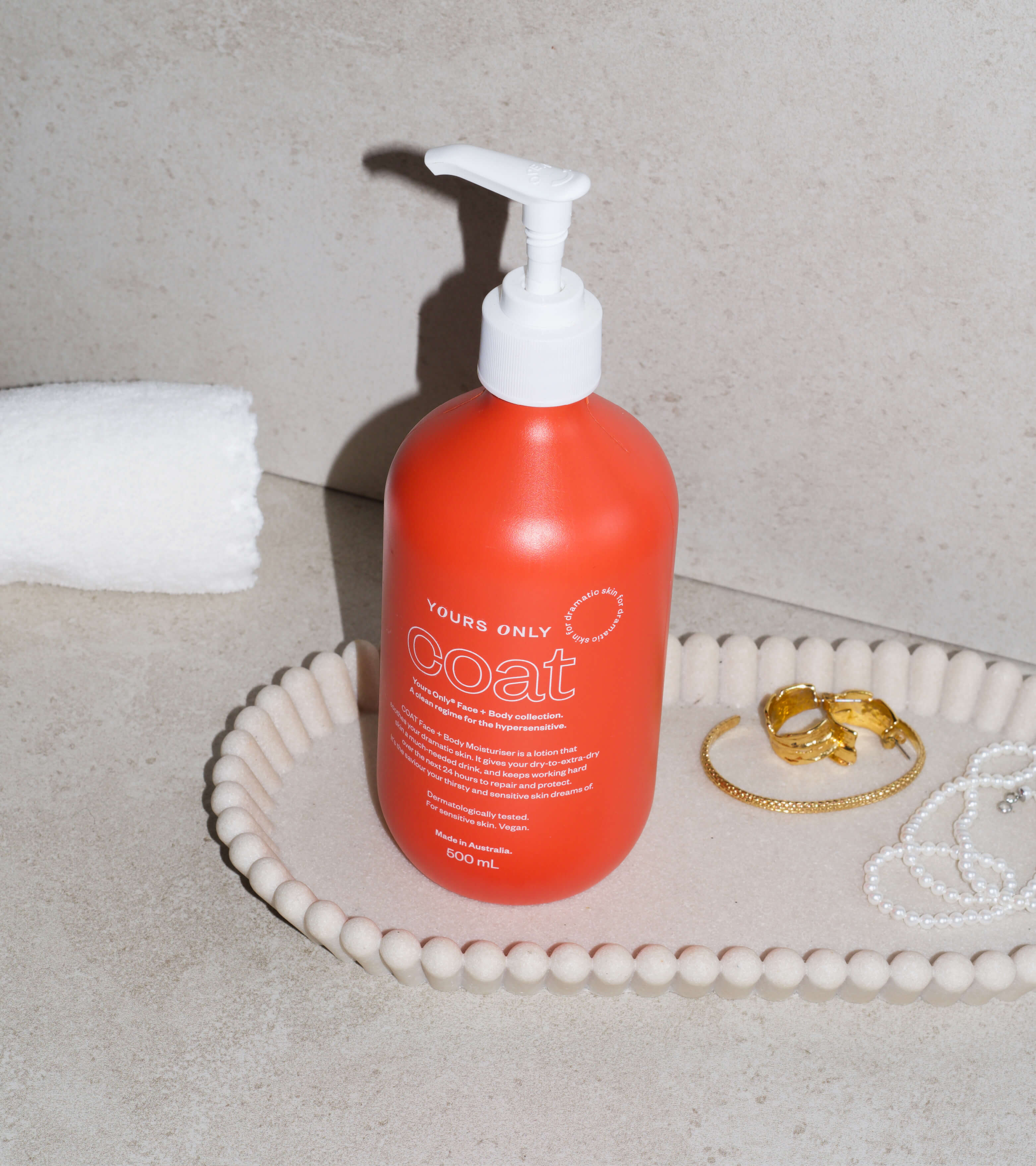 Yours Only Coat 500mL bottle on a tray with jewelry and a white towel
