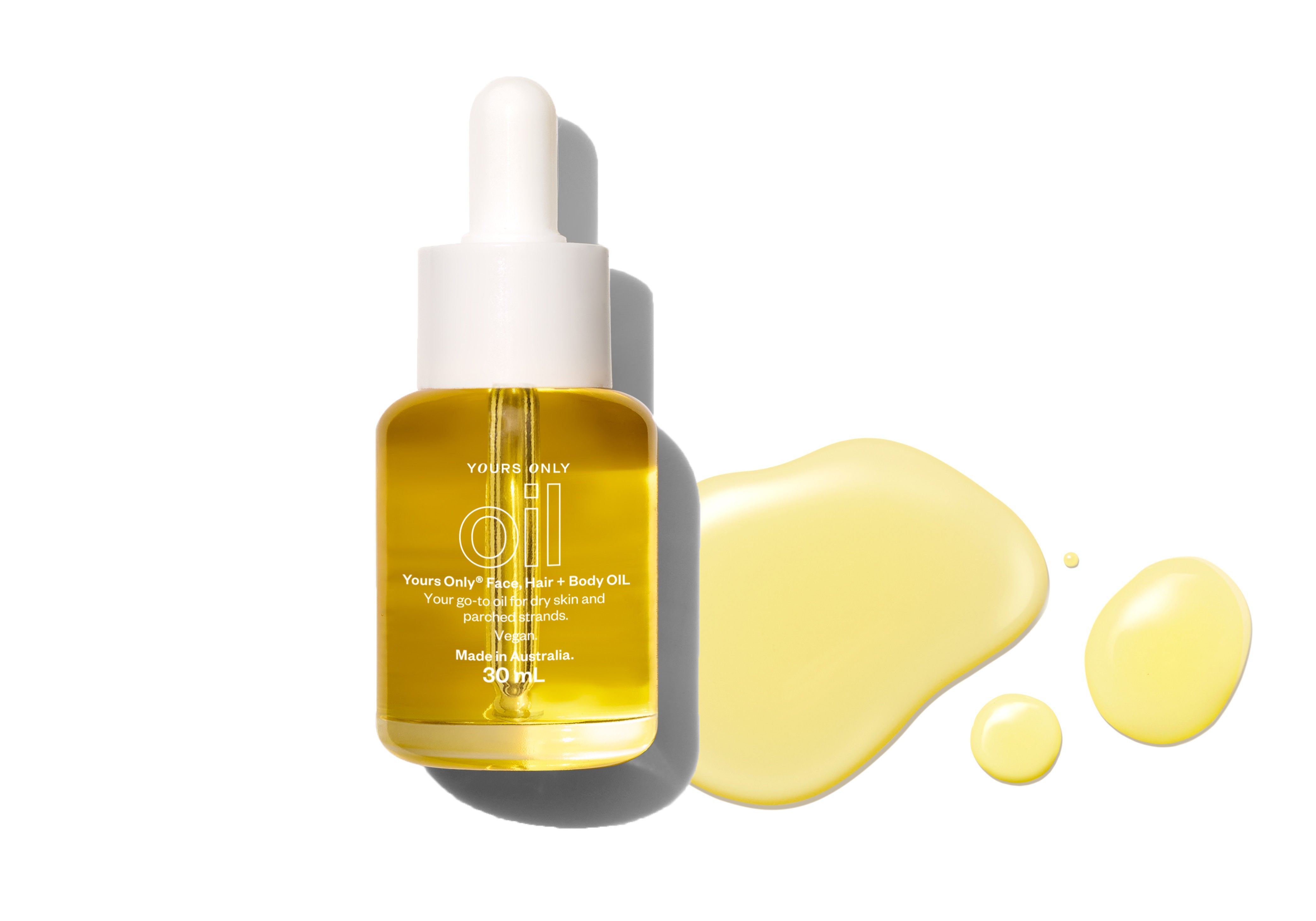 Yours Only Face, Hair + Body Oil in a dropper bottle with oil drops on a white surface