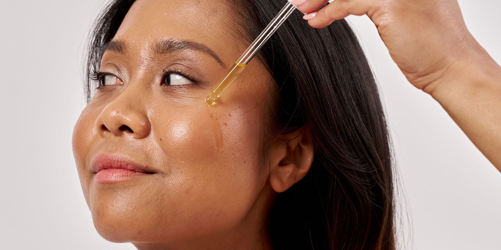 Woman applying serum to her cheek with a dropper
