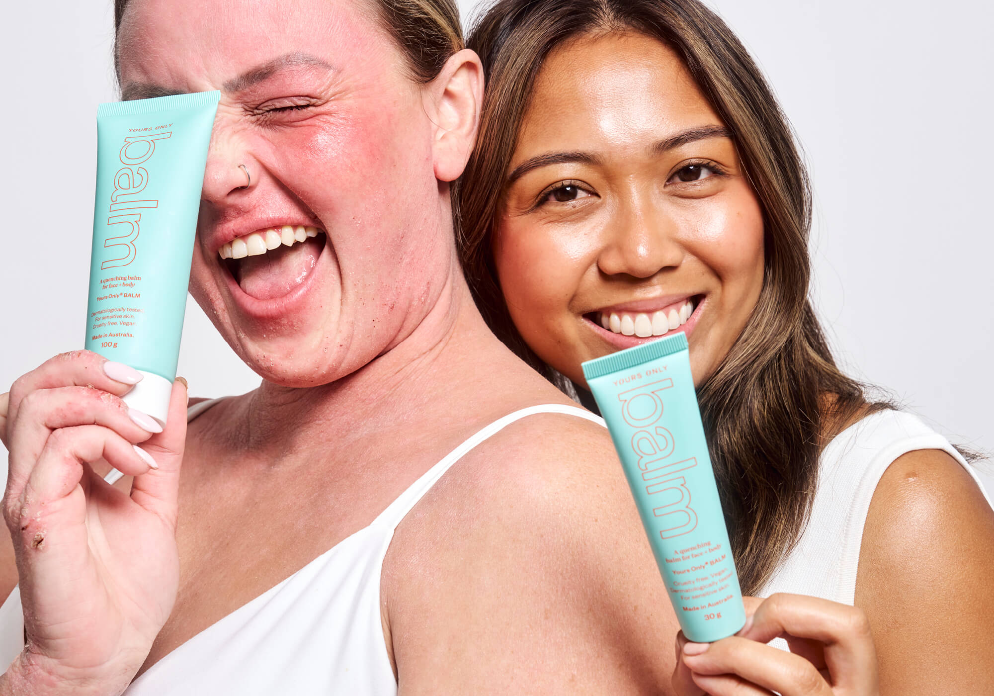 Two women holding Yours Only Balm tubes, one with red skin, the other with clear skin