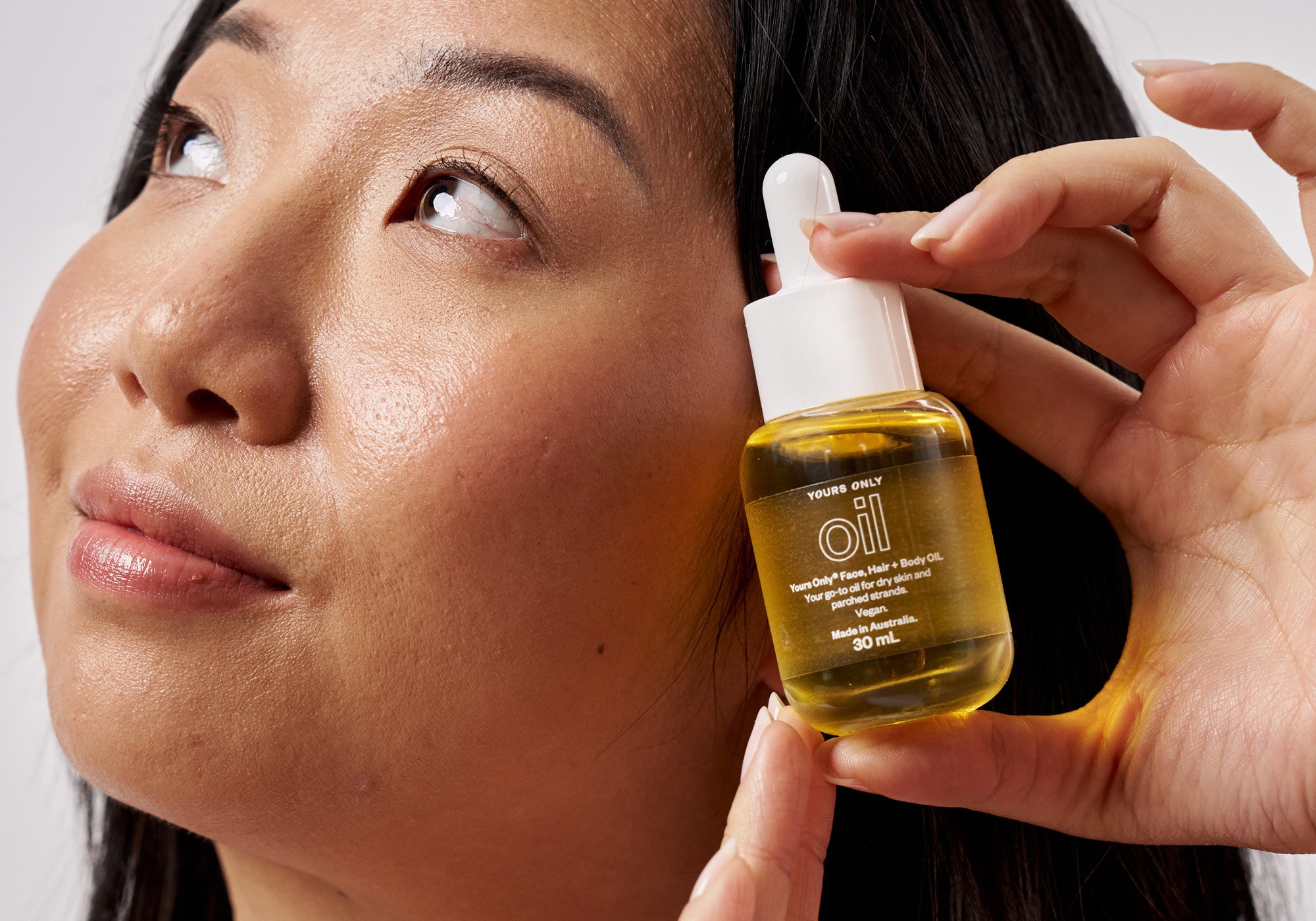 Woman holding a bottle of Yours Only Face, Hair + Body Oil with a dropper